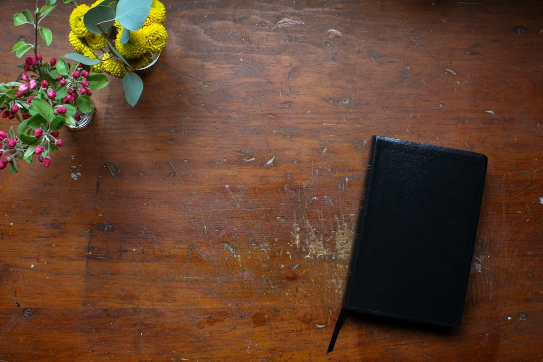 Schwarzes Buch auf einem Holztisch mit Blumen am Rand